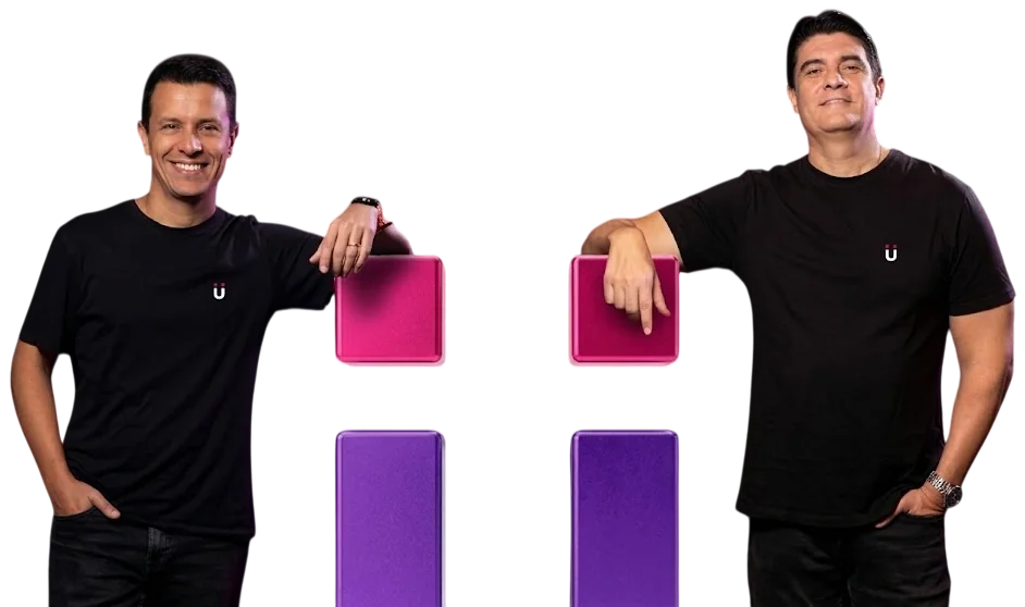 Fabiano César e Sérgio Carvalho, sócios da Pulsy Mídia, de camiseta preta com o “ü” da Pulsy, cada um apoiado num dos quadrados rosa do “ü” do logo da Pulsy